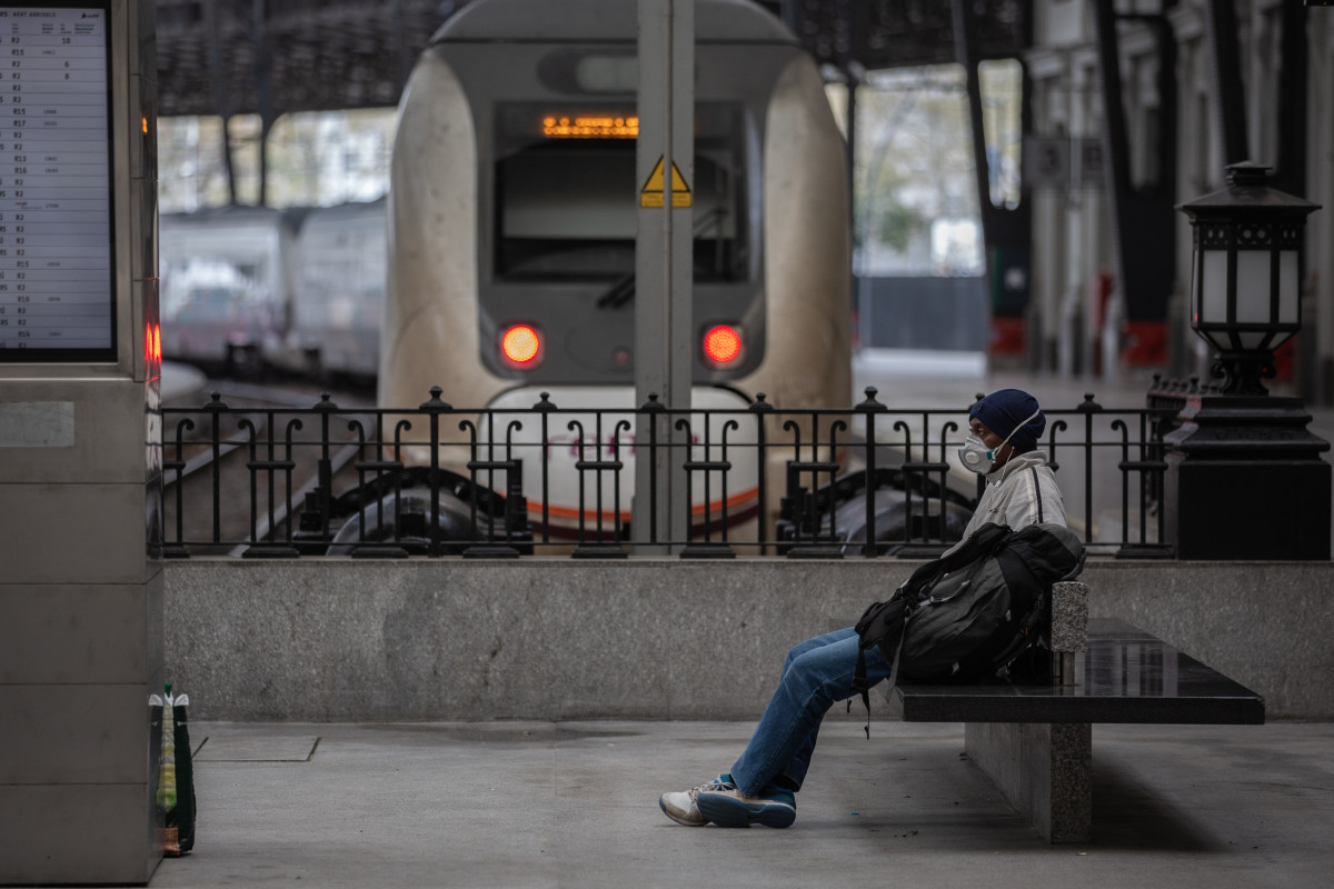 Un hombre protegido con una mascarilla espera sentado en un banco en una estación de tren de Barcelona durante el segundo día laborable del estado de alarma por el coronavirus, en Barcelona (España), a 17 de marzo de 2020.